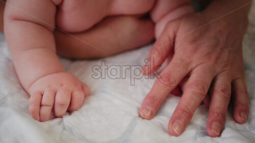 Close up of a tiny baby hand held by an adult finger on a soft surface