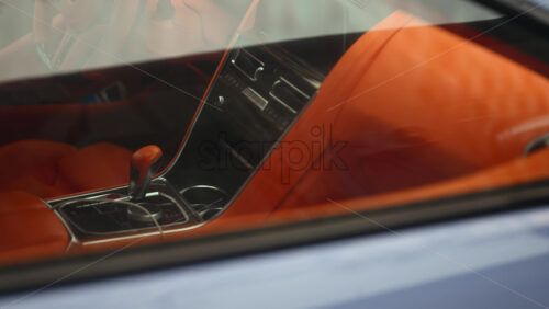 Close up view through a car window revealing a luxury vehicle interior with bright orange leather seats and modern dashboard design