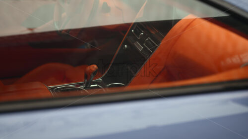 Close up view through a car window revealing a luxury vehicle interior with bright orange leather seats and modern dashboard design