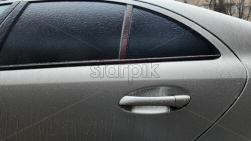 Side view of a car window covered in frost and ice, creating a textured frozen surface with urban background
