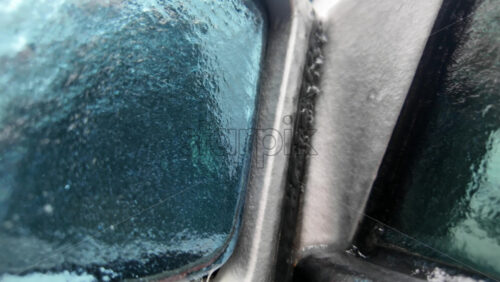 Close up of a car side mirror covered in ice and dripping meltwater