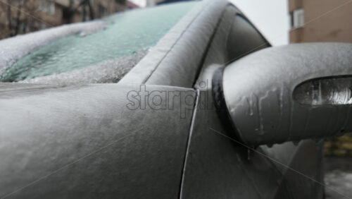 Close up of a car side mirror covered in ice and dripping meltwater