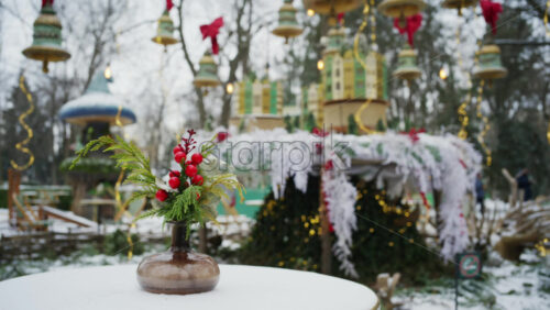 Close up of a decorative winter floral arrangement on a table, with a Christmas cafe scene and festive lights in the background