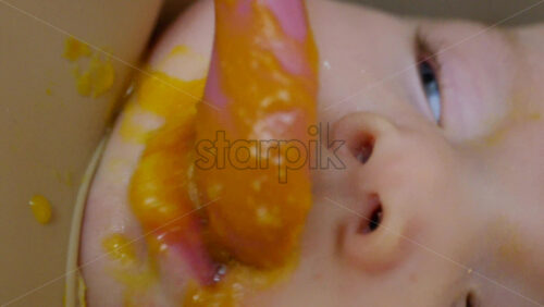 Close up of a baby being fed with a spoon, showing facial details and soft expressions. Vertical