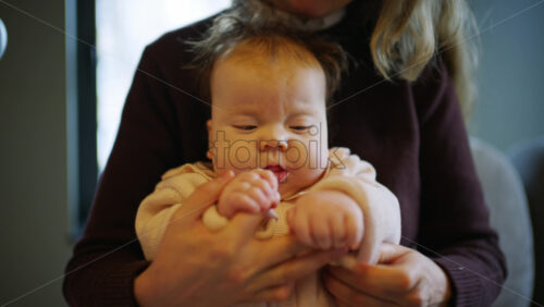 Close up of a baby sitting on an adult's lap indoors while gently holding hands