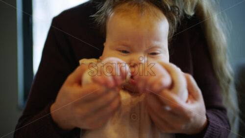 Close up of a baby sitting on an adult's lap indoors while gently holding hands