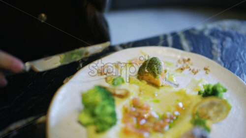Close up of a fork lifting broccoli from a plate with salmon and vegetables
