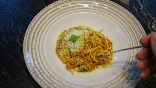 Close up of a fork lifting pasta covered with grated cheese from a plate at a restaurant