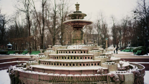 Static shot of a decorative stone fountain covered in snow inside a public park