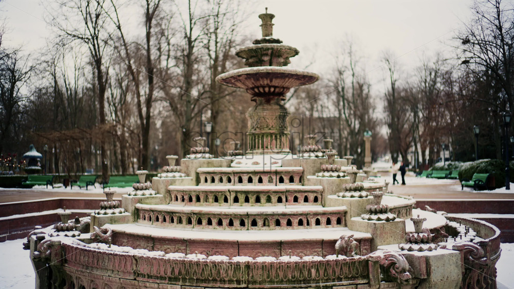 Static shot of a decorative stone fountain covered in snow inside a public park