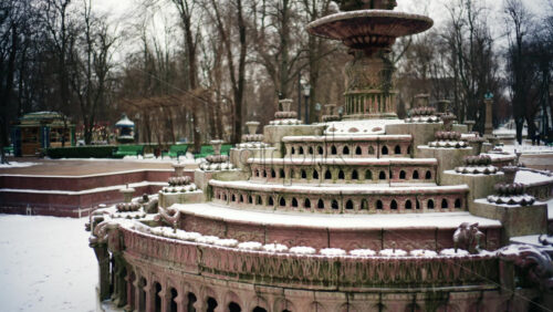 Static shot of a decorative stone fountain covered in snow inside a public park
