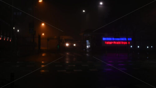 Out of focus view of a foggy urban intersection at night with neon signage and streetlights glowing through mist
