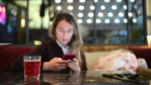 Woman seated indoors at a cafe table, focused on her smartphone
