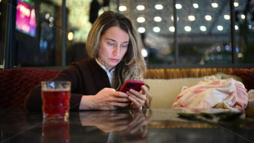 Woman seated indoors at a cafe table, focused on her smartphone