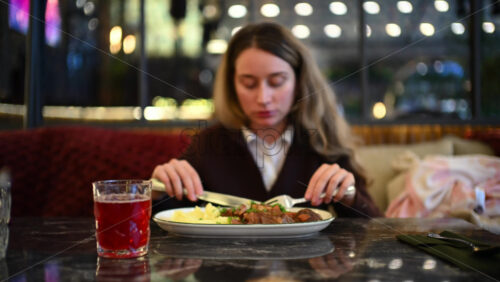 Woman eating mashed potatoes and meat at a restaurant table using fork and knife