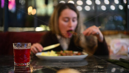 Woman eating mashed potatoes and meat at a restaurant table using fork and knife