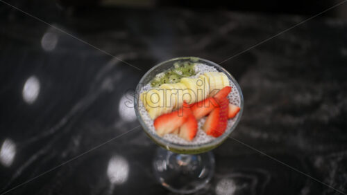 Close up of a chia pudding dessert served in a glass, topped with sliced strawberries and fruit puree