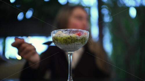 Woman eating a chia pudding dessert with fresh fruit toppings