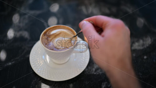 Close up of a female hand stirring cappuccino coffee in a white cup