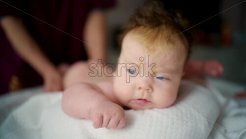 Close up of a baby lying on their stomach during tummy time while being gently supported by an adult