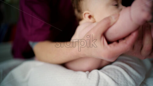 Close up of a baby lying on their stomach during tummy time while being gently supported by an adult