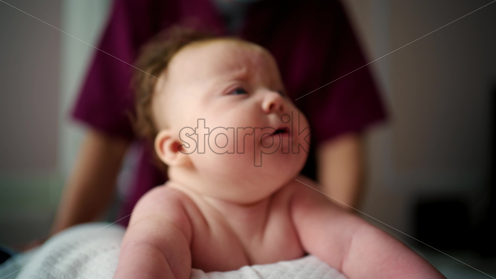 Close up of a baby lying on their stomach during tummy time while being gently supported by an adult