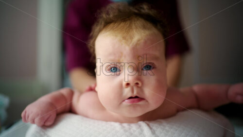 Close up of a baby lying on their stomach during tummy time while being gently supported by an adult