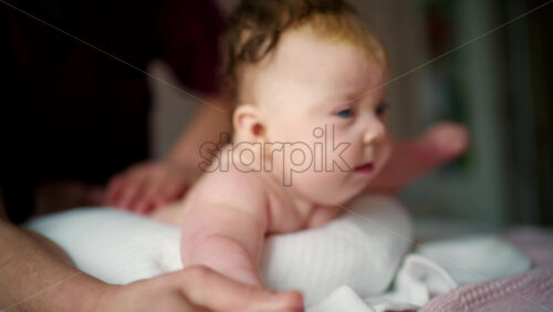Baby resting comfortably on a soft cushion while a caregiver remains close for support