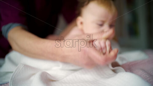 Close up of a baby lying on their stomach during tummy time while an adult gently supports the back and arms