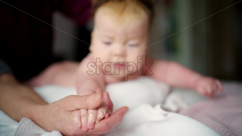 Close up of a baby lying on their stomach during tummy time while an adult gently supports the back and arms