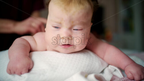 Close up of a baby lying on their stomach during tummy time while an adult gently supports the back and arms