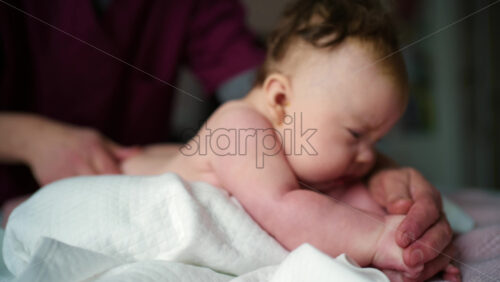 Side view of a baby resting on a soft cushion during tummy time while a caregiver's hands remain nearby for support