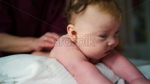 Side view of a baby resting on a soft cushion during tummy time while a caregiver's hands remain nearby for support