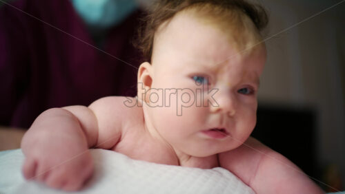 Side view of a baby resting on a soft cushion during tummy time while a caregiver's hands remain nearby for support