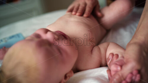 Baby lying on their back while an adult massages them and gently holds the baby's hand