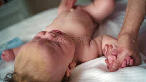 Baby lying on their back while an adult massages them and gently holds the baby's hand