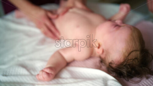 Baby lying on their back while an adult massages them and the mother gently holds the baby's hand