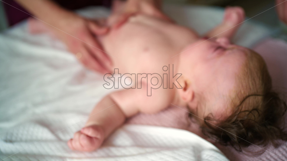 Baby lying on their back while an adult massages them and the mother gently holds the baby's hand