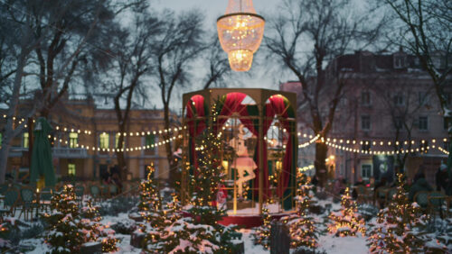 Wide view of a festive Christmas decoration with lights, at an outdoor cafe near small trees, and ornaments