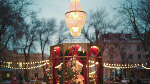 Wide view of a festive Christmas decoration with lights, at an outdoor cafe near small trees, and ornaments