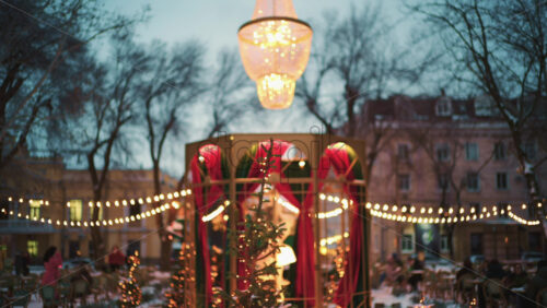 Wide view of a festive Christmas decoration with lights, at an outdoor cafe near small trees, and ornaments