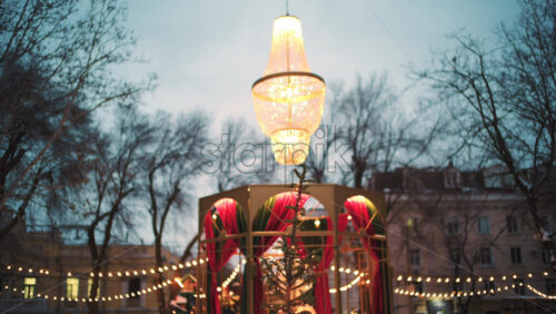 Wide view of a festive Christmas decoration with lights, at an outdoor cafe near small trees, and ornaments