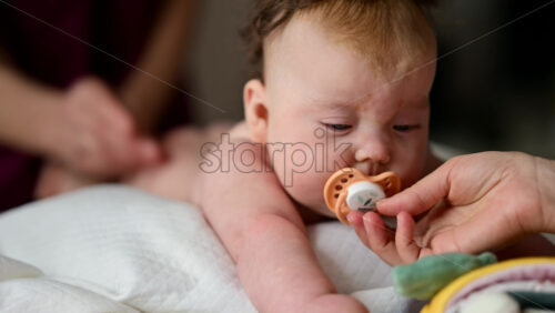 Cute baby lying on stomach during tummy time while interacting with a pacifier