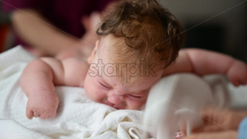 Woman trying to distract a crying baby lying on a blanket during massage with a soft toy