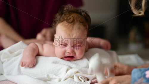 Woman trying to distract a crying baby lying on a blanket during massage with a soft toy