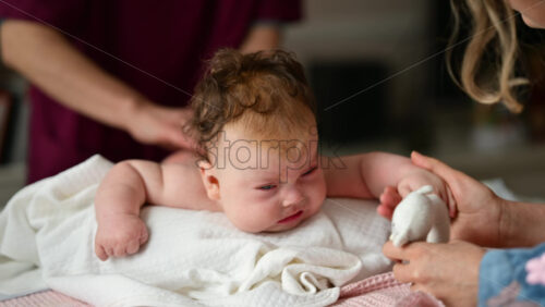 Woman trying to distract a crying baby lying on a blanket during massage with a soft toy