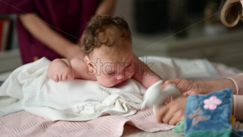 Woman trying to distract a crying baby lying on a blanket during massage with a soft toy