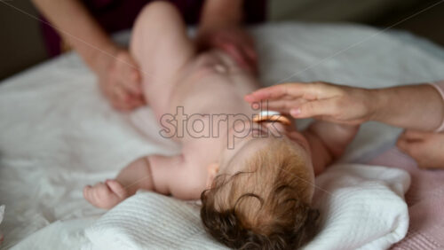 A newborn lying on a soft bed while a caregiver is massaging the baby