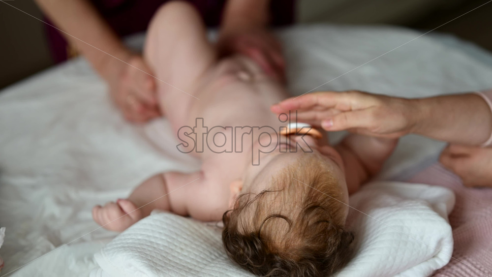 A newborn lying on a soft bed while a caregiver is massaging the baby