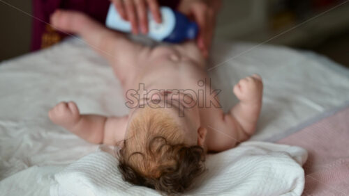 A newborn lying on a soft bed while a caregiver applies baby oil from a bottle and massaging the baby